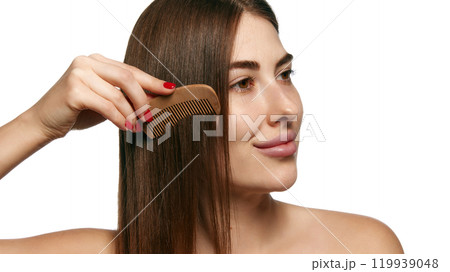 Woman combing her long hair with wooden comb, highlighting natural hair care against white background. Woman combing her long hair with wooden comb, highlighting natural hair care against white background. 119939048