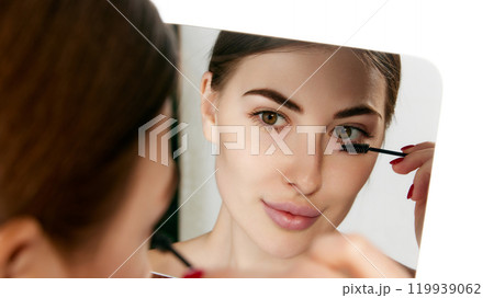 Close-up of woman applying mascara with focus on her eye, portraying daily beauty ritual against white background. 119939062