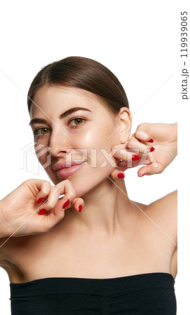 Close-up of young brunette woman massaging her jawline with both hands, emphasizing facial care against white background. Close-up of young brunette woman massaging her jawline with both hands, emphasizing facial care against white background. 119939065