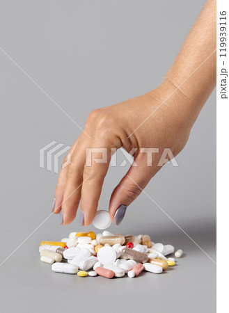 Woman hand put a pill on a pile of medical pills, tablets and capsules closeup against grey 119939116