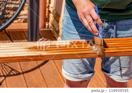 Close up male hands holding a brush and painting a rough varnish on the background of the surface of a wooden board 119939585