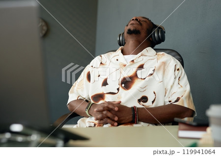 Portrait of bored African American man falling asleep in chair at workplace struggling to do work in office, copy space Portrait of bored African American man falling asleep in chair at workplace struggling to do work in office, copy space 119941064