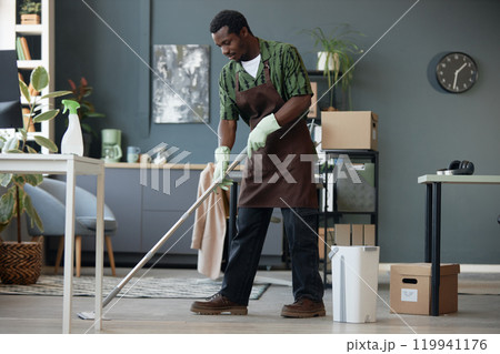 Full length side view of adult African American man mopping floors in office and enjoying Spring cleaning at workplace, copy space 119941176