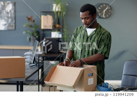 Waist up portrait of young African American man unpacking boxes on table in empty office, copy space Waist up portrait of young African American man unpacking boxes on table in empty office, copy space 119941209