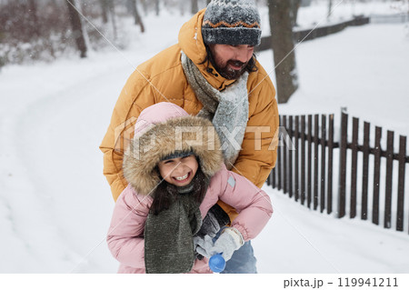 Portrait of carefree father and daughter covered in snow while playing together in winter park, copy space 119941211
