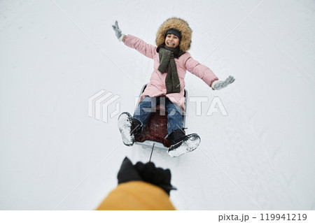 High angle view of cheerful young girl sledding in winter outdoors with fathers hand holding lead, copy space 119941219
