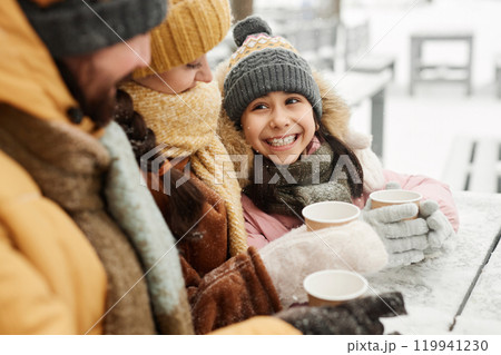 Portrait of happy young girl looking up at mother and father while enjoying hot cocoa at outdoor cafe in winter Portrait of happy young girl looking up at mother and father while enjoying hot cocoa at outdoor cafe in winter 119941230