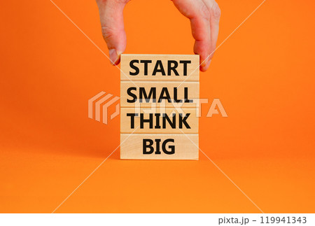 Start small think big symbol. Concept words 'Start small think big' on wooden blocks on a beautiful orange background. Businessman hand. Business, motivational and start small think big concept. Start small think big symbol. Concept words 'Start small think big' on wooden blocks on a beautiful orange background. Businessman hand. Business, motivational and start small think big concept. 119941343