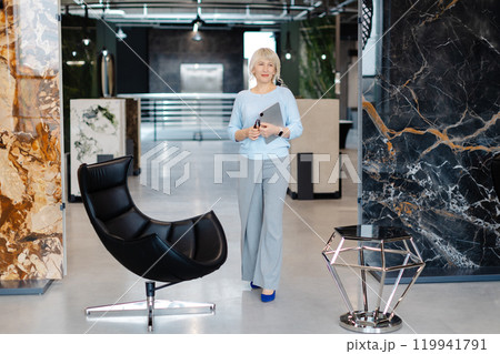 Confident Businesswoman Holding Tablet in Modern Office Setting Confident Businesswoman Holding Tablet in Modern Office Setting 119941791