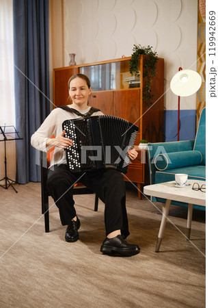 A middle-aged musician playing the accordion in a cozy living room during a bright afternoon 119942669