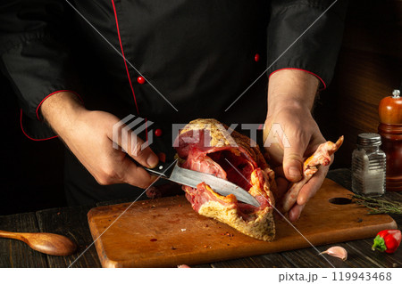 In the warm, cozy kitchen of the bar, an experienced chef confidently cuts duck meat, demonstrating culinary skills and the art of cooking 119943468