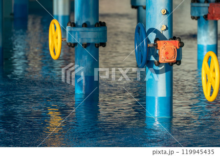 Pipes Valves Water - Industrial facility showing blue pipes with valves partially submerged in water. 119945435