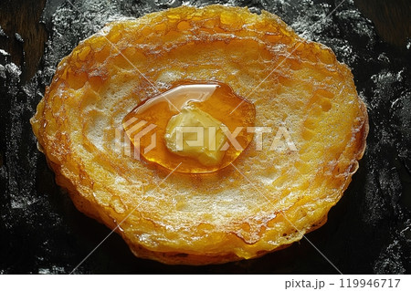 A close-up view captures a golden stack, emphasizing its crispy edges and fluffy center. Butter melts into the warm surface, while syrup pools invitingly, enhancing the dishs allure. 119946717