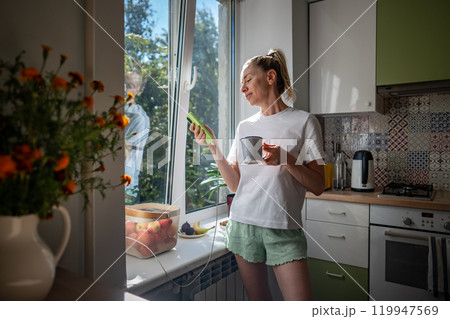 Lazy morning, procrastination with phone of woman drinking coffee in pajamas scrolling webs on phone 119947569