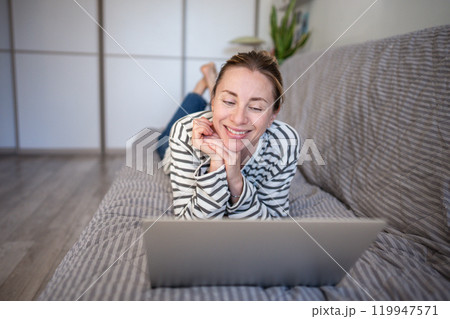 Happy middle aged woman have fun using laptop smiling lounging on couch watching interesting movie. Happy middle aged woman have fun using laptop smiling lounging on couch watching interesting movie. 119947571
