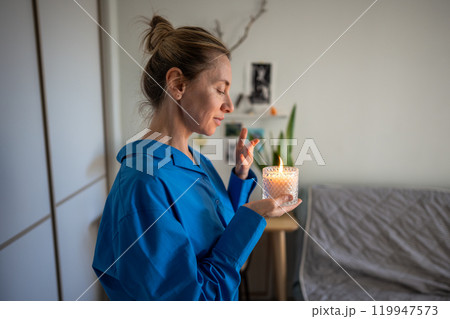 Calm woman enjoy smelling lighted scented candle, meditating, creating cozy atmosphere at home. Calm woman enjoy smelling lighted scented candle, meditating, creating cozy atmosphere at home. 119947573