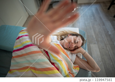 Portrait middle aged woman through palm smiling lying under blanket in bed awaked with good mood. 119947581