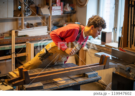 Carpenter with chisel check leather pads adhered to bed legs in workshop. Woodwork, small business Carpenter with chisel check leather pads adhered to bed legs in workshop. Woodwork, small business 119947602