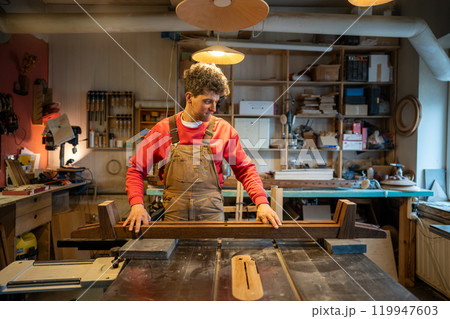 Content calm carpenter crafting wooden bed frame in workshop. Furniture from natural wood for sale Content calm carpenter crafting wooden bed frame in workshop. Furniture from natural wood for sale 119947603
