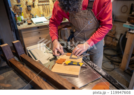 Carpenter work in furniture workshop, using ruler, caliper to cut leather for gluing to bed leg base 119947608