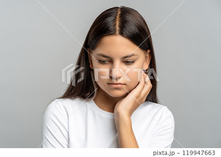 Shy schoolgirl avoiding eye contact, struggling with fear and insecurity, isolated in gray studio 119947663