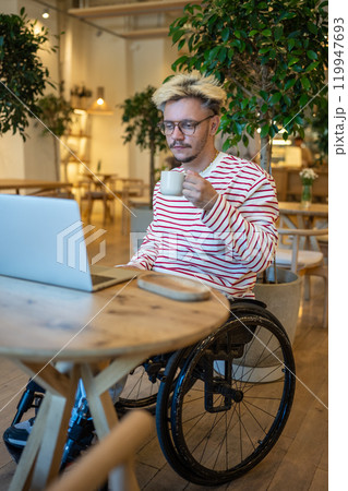 Focused guy freelancer with disabilities in wheelchair working online using laptop sits in cozy cafe Focused guy freelancer with disabilities in wheelchair working online using laptop sits in cozy cafe 119947693