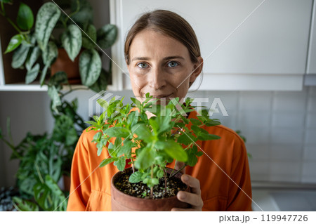 Smiling woman holding flower pot with fresh green mint grown at home, looking at camera. Hobby. 119947726
