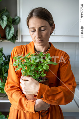 Contented, calm woman hugs pot of fragrant herb mint grown in home garden on windowsill. Plant lover 119947738