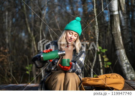 Woman hiker having break drinking tea sitting on wooden path in autumn park in Scandinavia. Woman hiker having break drinking tea sitting on wooden path in autumn park in Scandinavia. 119947740