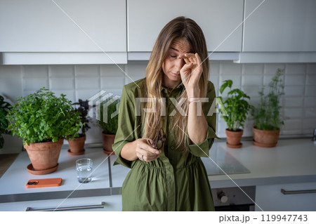 Sleepy tired woman suffering from insomnia rubbing eyes on kitchen with houseplants early morning. Sleepy tired woman suffering from insomnia rubbing eyes on kitchen with houseplants early morning. 119947743