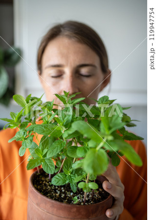 Woman with closed eyes enjoying smelling green mint plant growing it at home. Green hobby 119947754