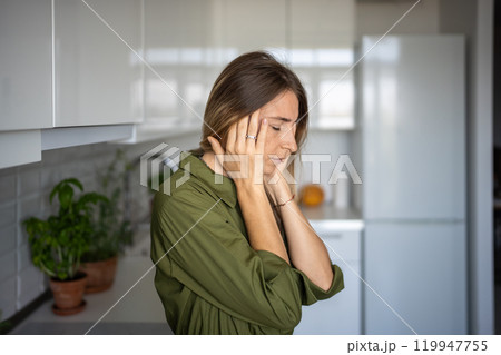 Tired woman feeling headache rubbing temples standing on kitchen with closed eyes. Tired woman feeling headache rubbing temples standing on kitchen with closed eyes. 119947755