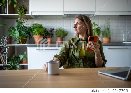 Thoughtful woman drinking tea during work break, looking at window, planning future working process Thoughtful woman drinking tea during work break, looking at window, planning future working process 119947766
