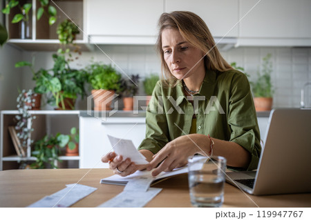 Freelance accountant working at home comparing figures in bills and financial document in laptop Freelance accountant working at home comparing figures in bills and financial document in laptop 119947767