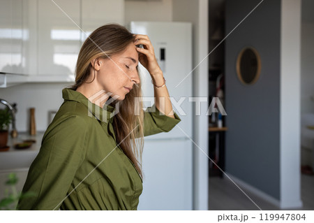 Tired woman feels pain in head holds forehead standing at home with closed eyes focus on sensations 119947804