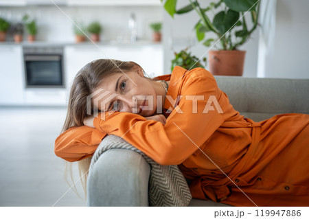 Portrait of relaxed woman lying on sofa with head bowed on armrest look at camera with calm emotion. 119947886