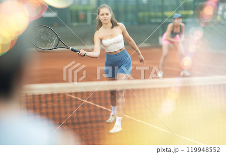 Two young women playing doubles tennis Two young women playing doubles tennis 119948552