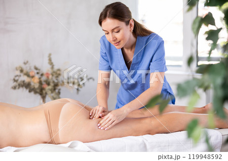 Female masseur makes anti-cellulite massage of thighs and legs to woman 119948592