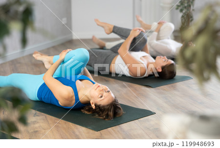 Woman doing Ardha Pawanmuktasana with group in yoga studio 119948693