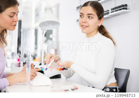 Young female manicurist showing palette of nail varnishes to woman client 119948713