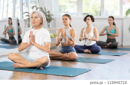 Senior woman meditating in Padmasana during group yoga class Senior woman meditating in Padmasana during group yoga class 119948728