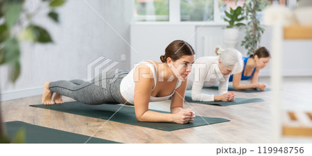 Young woman holding forearms plank pose in yoga studio 119948756