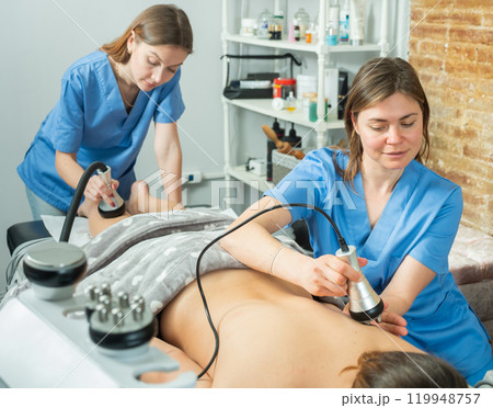 Professional cosmetologists performing electroporation procedure for female patient 119948757