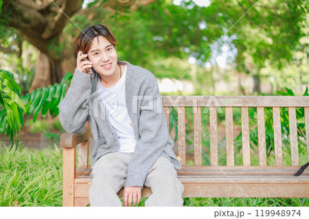 公園のベンチに座って電話をする日本人男性 119948974