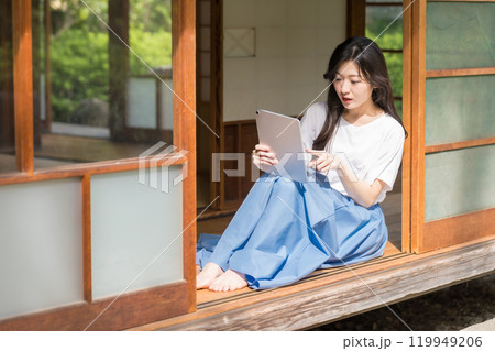 古民家の縁側でタブレットでネットショッピングを楽しむ若い女性 119949206