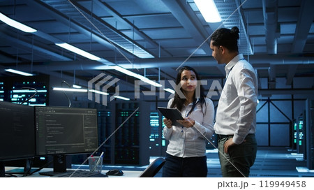 Team of technicians working on tablets in data center used for managing gear energy consumption. Teamworking colleagues using devices in workspace used for automation in server farm, camera B 119949458