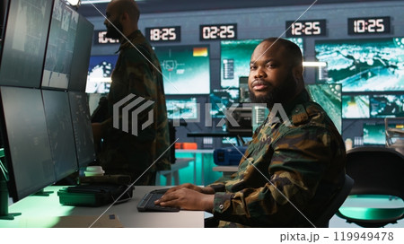 Army operative in command center analyzing surveillance data during global warfare. Intelligence agent in base of operations completes mission during World War 3 geopolitical operation, camera B 119949478