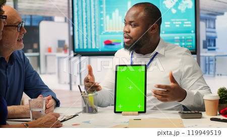 Adviser shows green screen on a tablet to middle aged people in modern office, meeting to discuss retirement and pension plan. Financial expert broker helping senior couple with finances. Camera A. 119949519