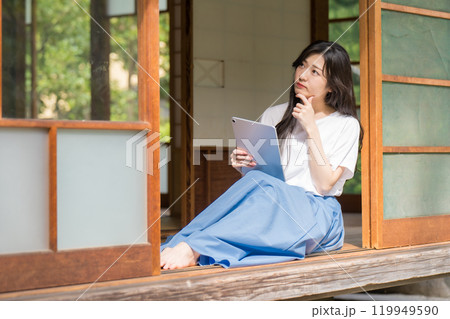 古民家の縁側でタブレットを見ながら悩む若い女 119949590