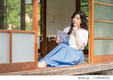 古民家の縁側でタブレットを見ながら悩む若い女 古民家の縁側でタブレットを見ながら悩む若い女 119949591